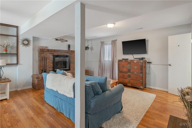 living room featuring a brick fireplace, light wood-style flooring, and baseboards