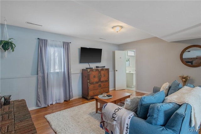 living area with light wood-style floors, a wainscoted wall, and visible vents