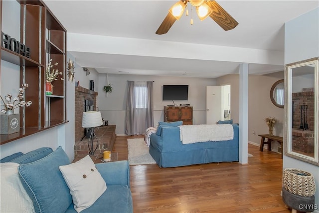 living area featuring ceiling fan, a brick fireplace, wood finished floors, and baseboards