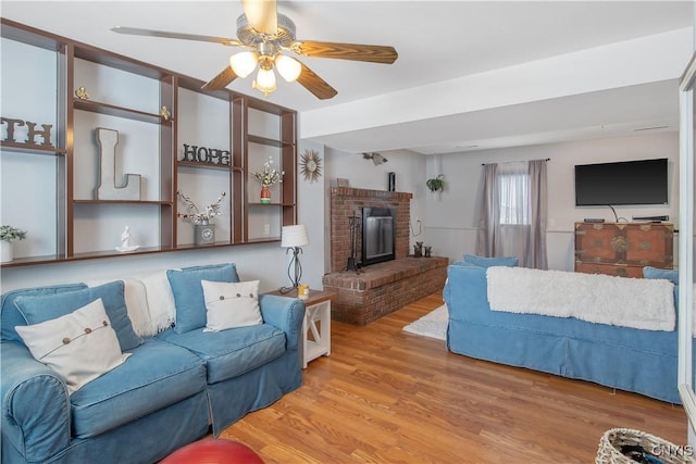 living room featuring a fireplace, a ceiling fan, and wood finished floors