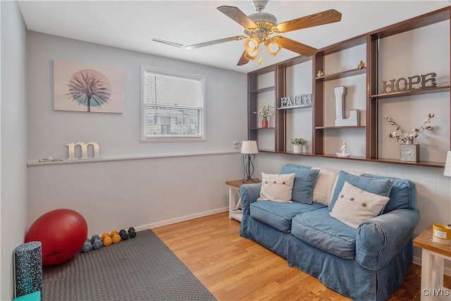 living area featuring baseboards, wood finished floors, visible vents, and a ceiling fan