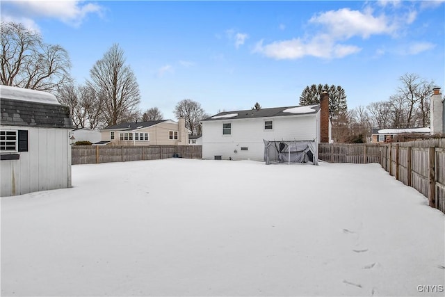 snow covered rear of property with a fenced backyard, an outdoor structure, and a chimney