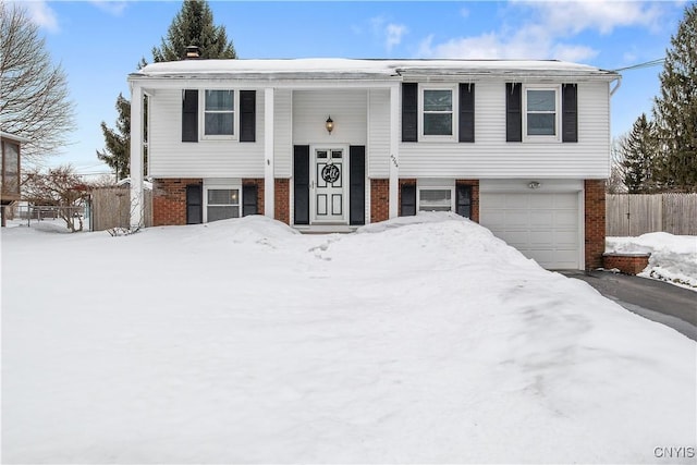 raised ranch with a garage, brick siding, and fence