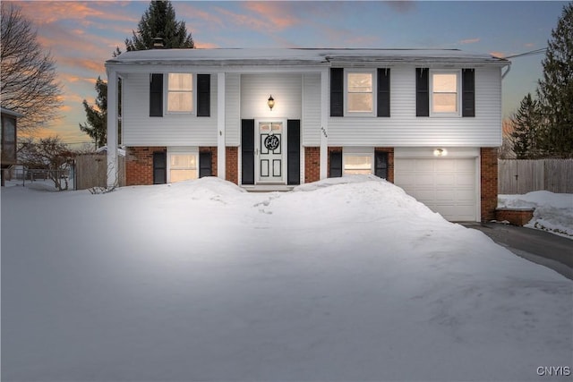 split foyer home featuring a garage, fence, and brick siding