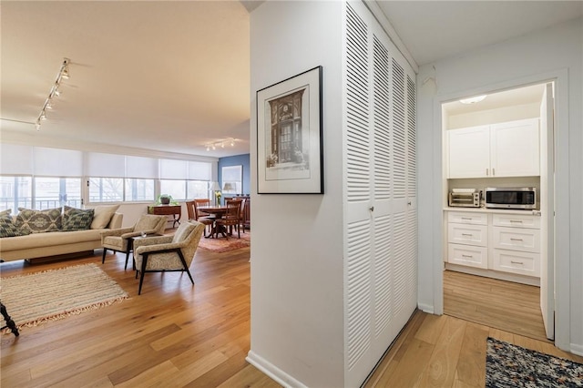 hallway featuring track lighting, baseboards, a toaster, and light wood finished floors