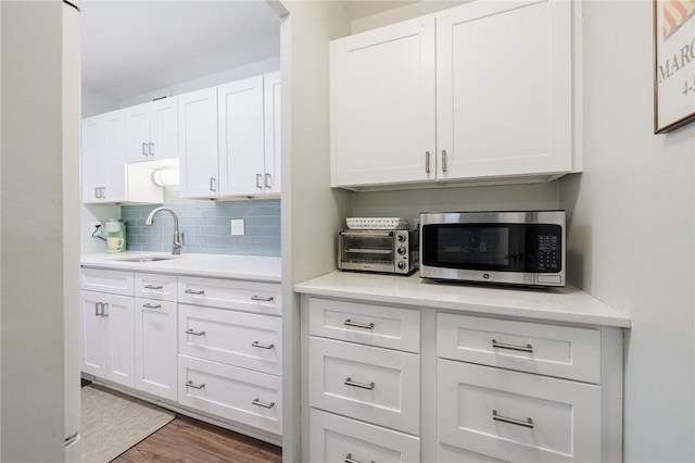 kitchen with light countertops, stainless steel microwave, a sink, and decorative backsplash