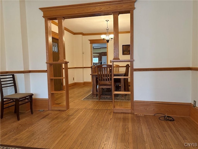 dining room with baseboards, wood-type flooring, crown molding, ornate columns, and a chandelier