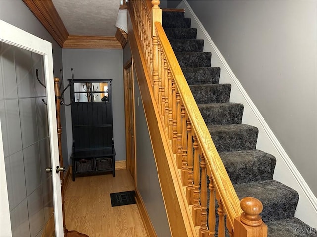 staircase with baseboards, visible vents, crown molding, and wood finished floors