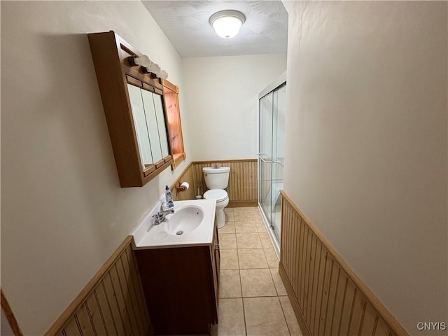 full bath with a stall shower, tile patterned flooring, a wainscoted wall, and toilet