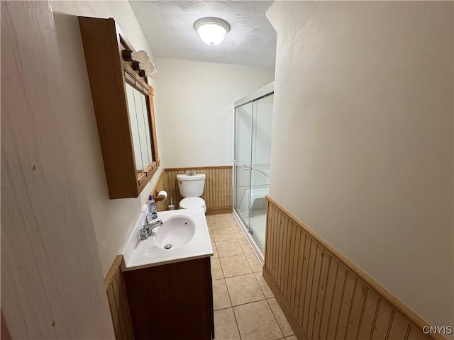 full bath with toilet, a stall shower, wainscoting, vanity, and tile patterned floors