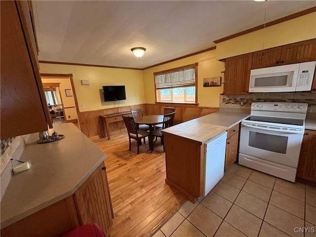 kitchen with a peninsula, white appliances, light countertops, ornamental molding, and wainscoting