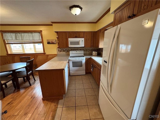 kitchen with a peninsula, white appliances, light countertops, ornamental molding, and wainscoting