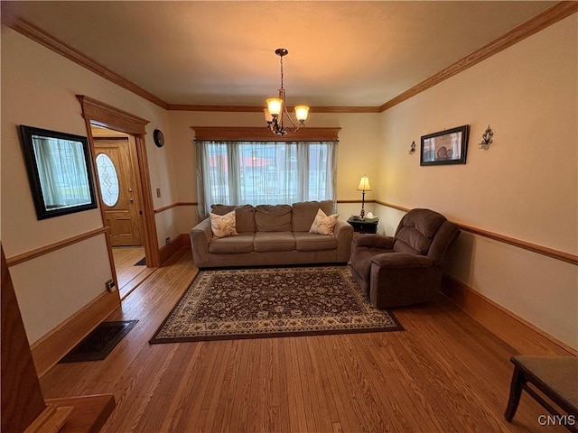 living room featuring baseboards, visible vents, ornamental molding, wood finished floors, and a chandelier