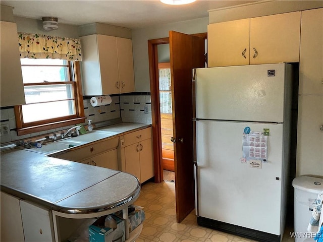 kitchen with a sink, light countertops, backsplash, freestanding refrigerator, and light floors