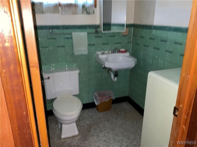 bathroom with toilet, tile walls, a sink, and wainscoting