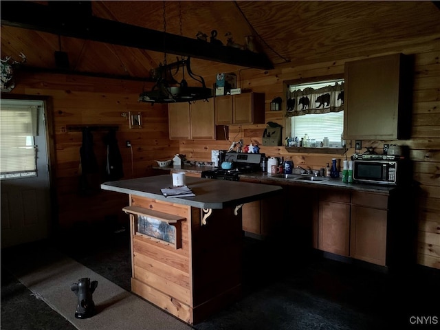 kitchen featuring wooden walls, dark countertops, a center island, black microwave, and gas stove