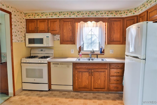 kitchen featuring brown cabinets, white appliances, a sink, and wallpapered walls