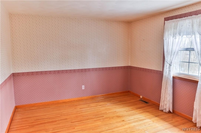 spare room with light wood-type flooring, visible vents, baseboards, and wallpapered walls