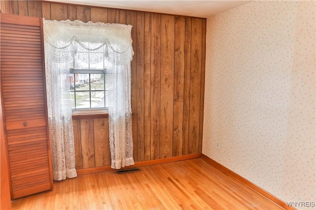 spare room featuring baseboards, visible vents, light wood finished floors, and wallpapered walls