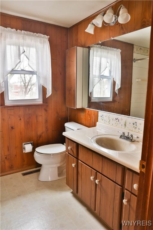 bathroom featuring visible vents, wooden walls, toilet, and vanity