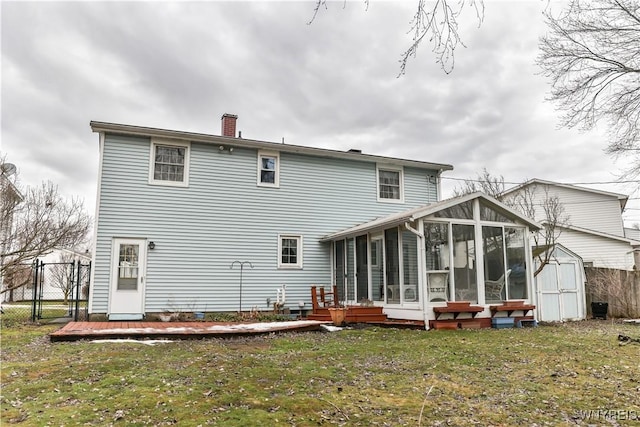 rear view of property featuring an outbuilding, fence, a sunroom, a shed, and a chimney