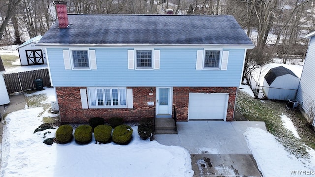 colonial-style house featuring an attached garage, a chimney, fence, and brick siding