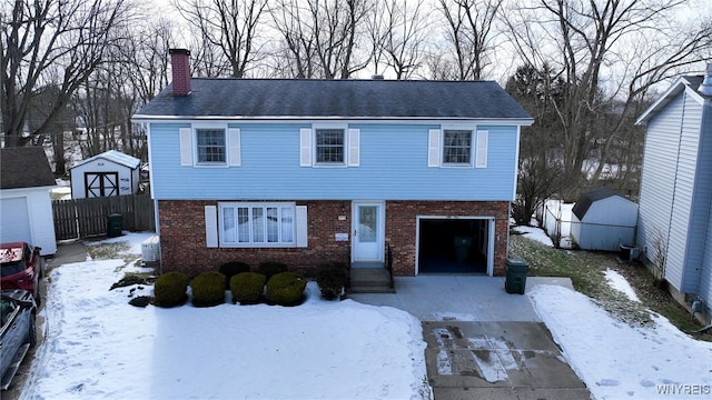 colonial house featuring a garage, driveway, a chimney, fence, and brick siding