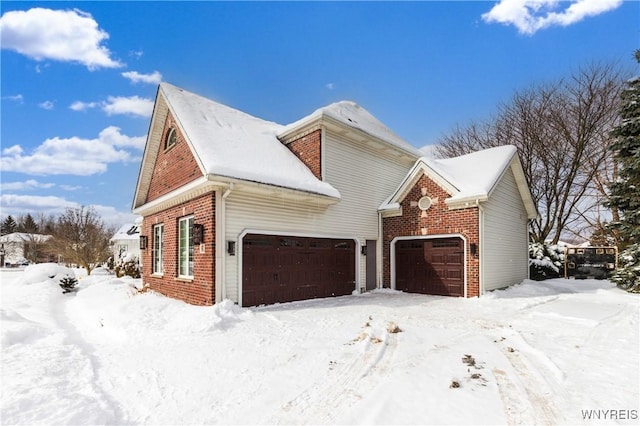 snow covered property with an attached garage and brick siding