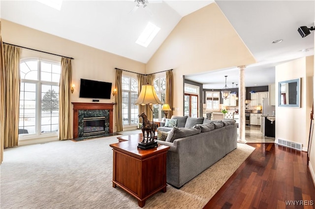 living area featuring high vaulted ceiling, a premium fireplace, visible vents, dark wood finished floors, and decorative columns