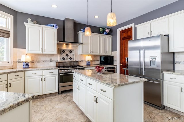 kitchen with light stone countertops, wall chimney range hood, appliances with stainless steel finishes, and decorative light fixtures