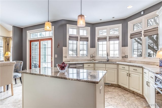 kitchen with light stone counters, decorative light fixtures, stainless steel appliances, a sink, and a kitchen island