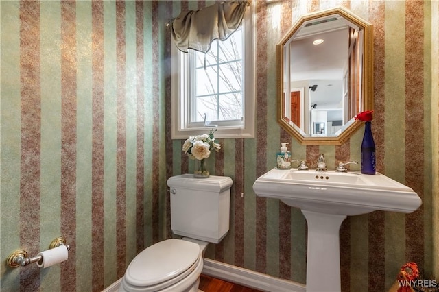 half bath featuring baseboards, toilet, and wallpapered walls