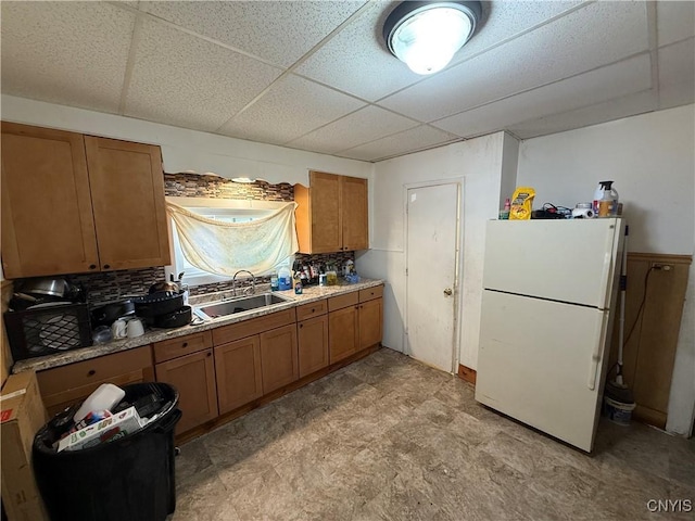 kitchen with tasteful backsplash, brown cabinetry, freestanding refrigerator, a paneled ceiling, and a sink