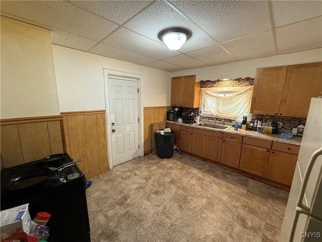 kitchen featuring wainscoting, brown cabinets, light countertops, a paneled ceiling, and a sink