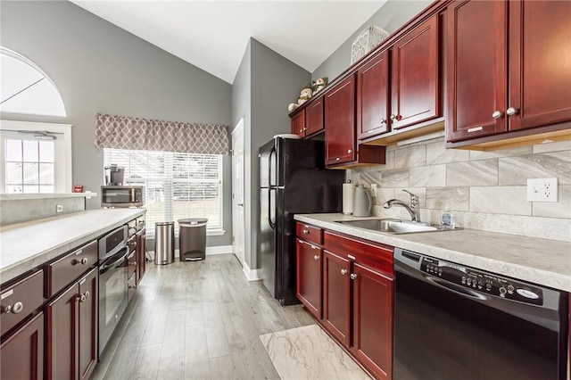 kitchen with reddish brown cabinets, vaulted ceiling, a sink, and black appliances