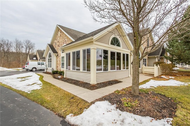 view of side of home with stone siding, driveway, and a sunroom