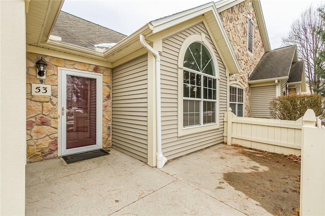 property entrance with stone siding, fence, and roof with shingles