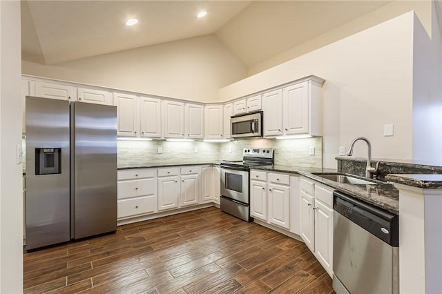 kitchen with dark stone counters, dark wood-style flooring, a peninsula, stainless steel appliances, and a sink