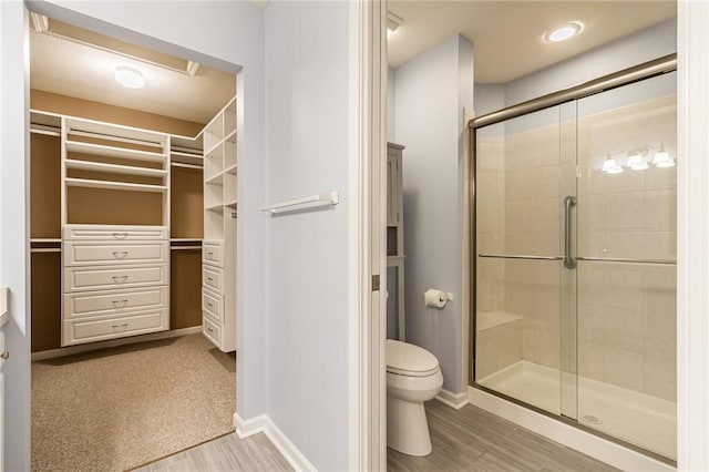 full bath with toilet, wood finished floors, baseboards, a shower stall, and a walk in closet