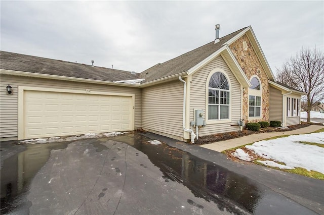 view of home's exterior with an attached garage, stone siding, and aphalt driveway