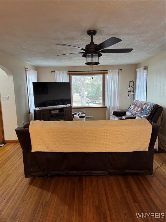 living room featuring arched walkways, a textured ceiling, wood finished floors, and a ceiling fan