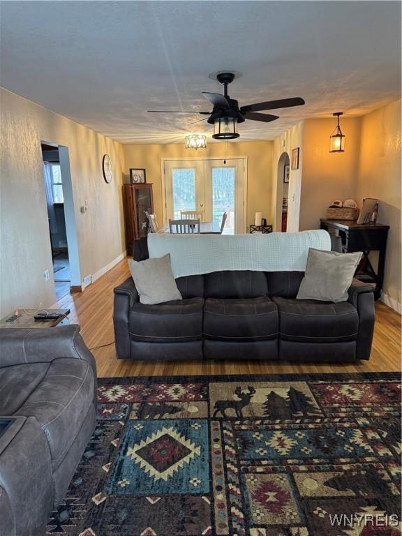 living area featuring ceiling fan, baseboards, arched walkways, and wood finished floors