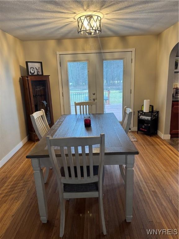 dining room with baseboards, arched walkways, wood finished floors, a textured ceiling, and french doors