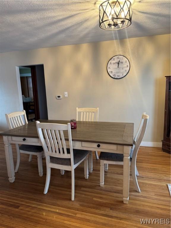 dining space with a textured ceiling, a chandelier, wood finished floors, and baseboards