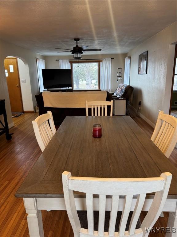 dining area featuring baseboards, ceiling fan, arched walkways, and wood finished floors