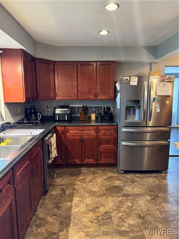 kitchen featuring stainless steel appliances, reddish brown cabinets, stone finish floor, and dark countertops