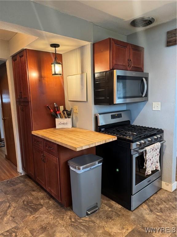 kitchen featuring stainless steel appliances, baseboards, wooden counters, stone finish floor, and decorative light fixtures