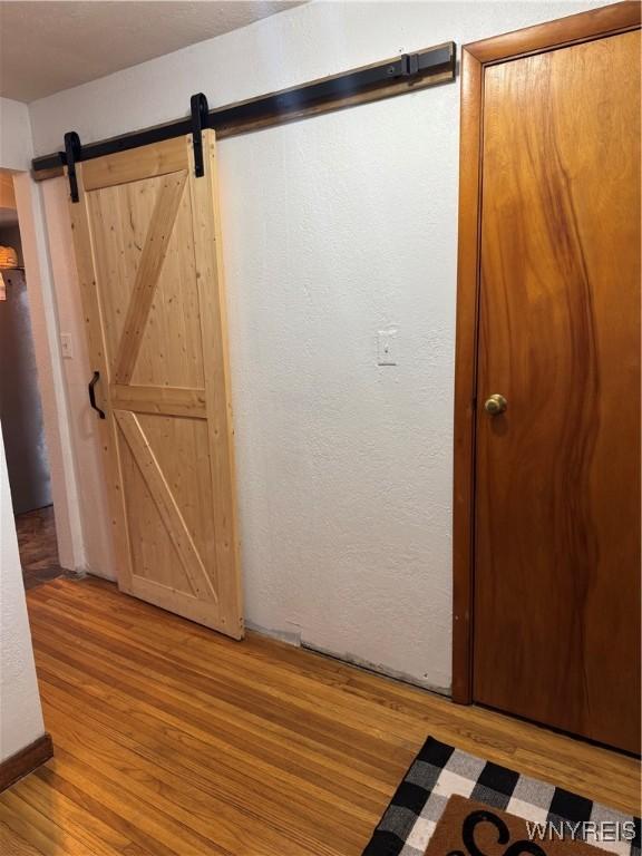 interior space with a textured wall, a barn door, and wood finished floors