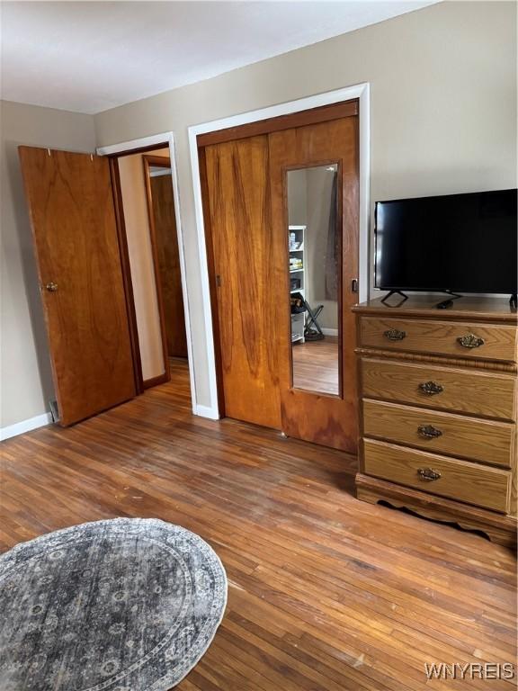 bedroom with two closets, baseboards, and wood finished floors