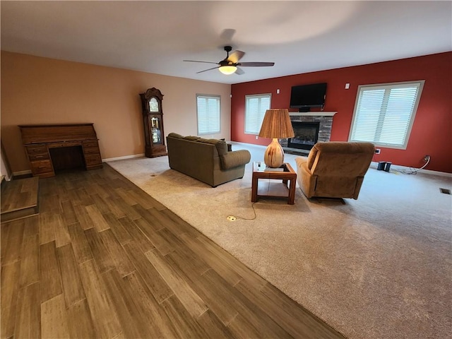 living area with a fireplace, wood finished floors, visible vents, a ceiling fan, and baseboards